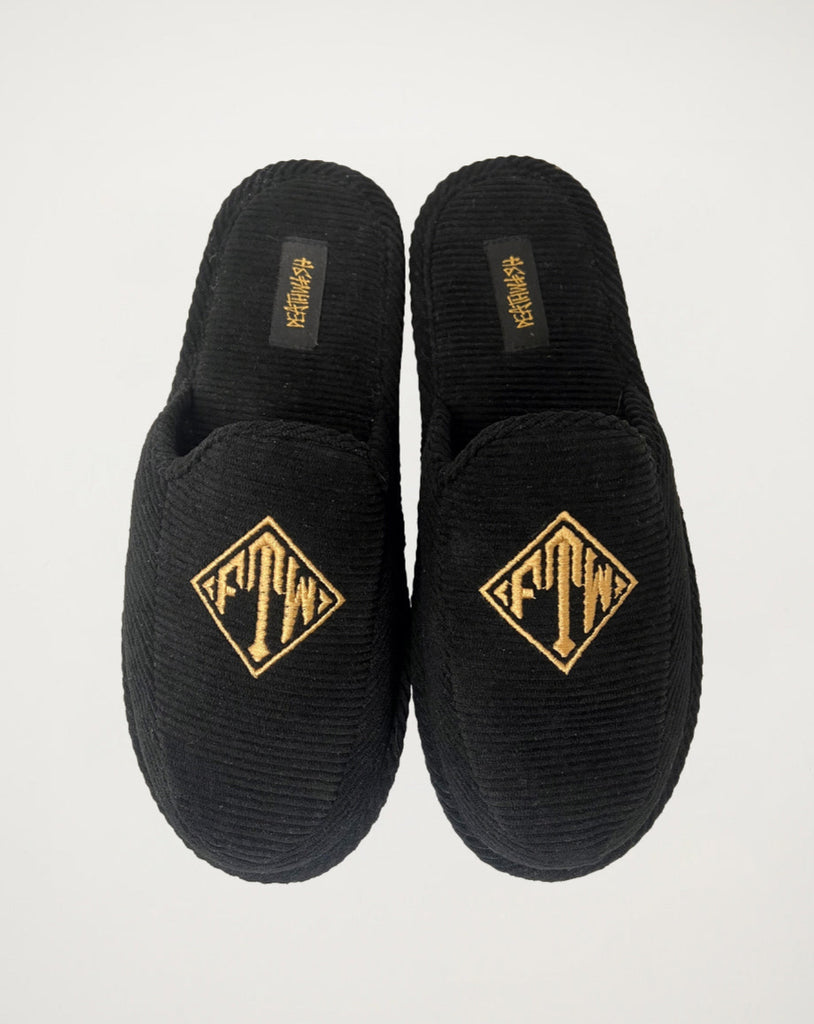 Black slippers with gold logo on a light gray background